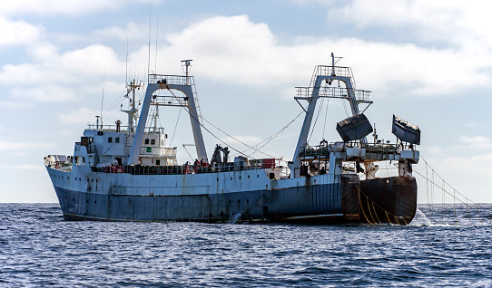 Large fishing trawler is fishing for fish and seafood in the ocean. Fishing vessel lifts a trawl tackle off the southern tip of Africa.