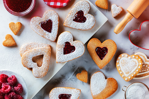 Christmas or Valentine's Day traditional homemade heart shaped cookies, delicious snack. Top view of traditional heart-shaped Linzer cookies with raspberry jam on the white marble table. Close up, flat lay.