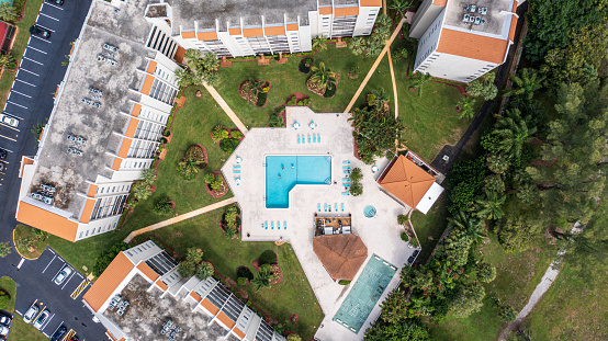 The aerial drone shot over the swimming pool is within an apartment complex on a sunny day in Fort Lauderdale, Florida.