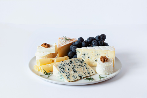 Cheese plate served with grapes and walnuts on a grey concrete background
