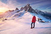 Young woman in snowy mountains at sunset in winter. Landscape with beautiful girl on the hill, snow covered rocks, colorful sky the evening. Mountain pass Passo Giau, Dolomites, Italy. Tourism. Travel