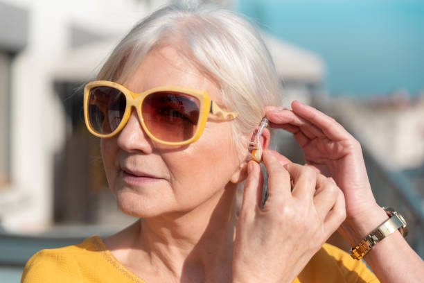 Senior woman puts on the hearing aid stock photo