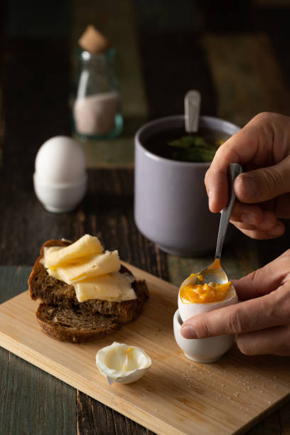 Still life breakfast. Boiled egg, homemade bread, tea with mint, salt, hand holds a spoon. Front view.