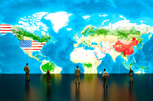 Businessman/politician figurines examine satellite view USA and China maps.