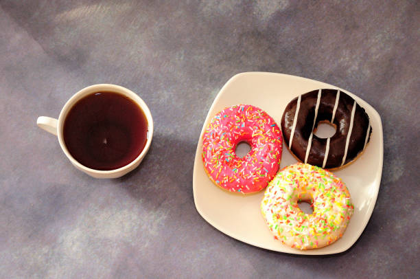 istock Three donuts in multicolored glaze on a plate and a cup of black tea. 1355581762