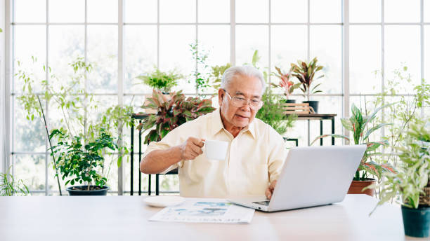 istock A senior retired old man dressed in casual style is using a laptop and drinking coffee while sitting at home with an indoor garden in the background. Retirement hobby and lifestyle. 1355584786