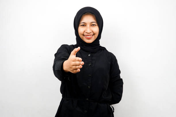Beautiful young asian muslim woman smiling confidently, with hands shaking the camera, hands sign of cooperation, hand sign of agreement, hand sign of friendship, isolated on white background stock photo