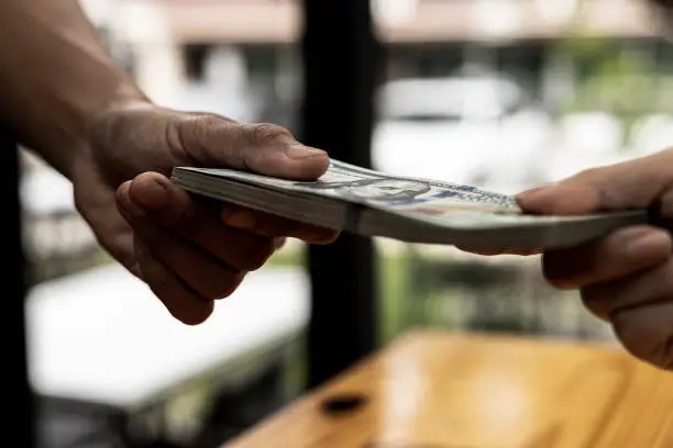 Photo of Two people are handing each other dollar bills, they are mutually beneficial business partners, they commit bribery fraud for business interests. The concept of corruption and bribery.