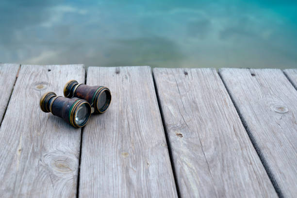 Binoculars on the background of wooden boards on the lake shore. Background for travel, tourism, navigation and search. vintage vintage binoculars on a wooden background at the water's edge glass, touristic, tourism, travel, old, nostalgia, exploration, trip, equipment, fence, lens, scope, geography, creative, wood, copy space, vacation, top view, hiking, direction, antique, view, sea, instrument, camping, navigation, adventure, ancient, binocular, outdoor, optical, object, weekend, hipster, overhead, retro, vintage, telescope, space, texture, design, concept, wooden, closeup, background, binoculars, route, wooden background, hobbies, search binoculars point of view stock pictures, royalty-free photos & images