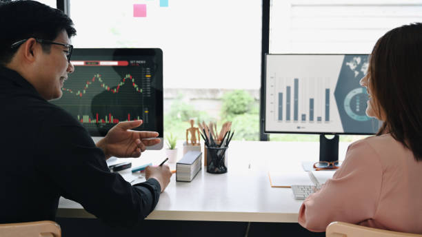 istock Rear view team of stock trader checking and analyzing financial graph on computer together in office. 1355590145