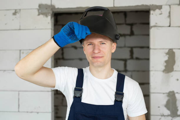 istock Male construction worker wearing a welding helmet and blue gloves against a brick wall. 1355593879