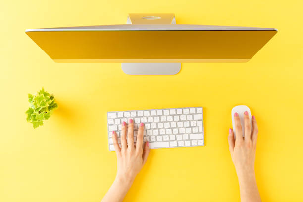 Female hands using modern computer with accessories on yellow background. Office desktop. Top view stock photo