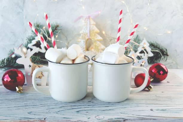 istock Cups of coffee with marshmallows, fir branches, Christmas decorations and illumination on a wooden table 1355596281