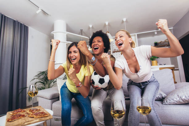 Group of cheerful female friends watching soccer match and celebrating victory at home. stock photo