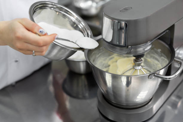 istock Pastry chef in the kitchen adds sugar to the kitchen machine, mixer. 1355597158