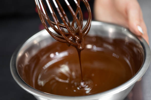 chef pastelero bate chocolate derretido en un tazón con un batidor de alambre de metal de cerca - brown chocolate candy bar close up fotografías e imágenes de stock