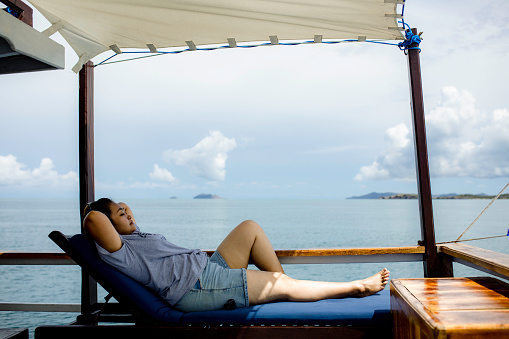 Back view of a young girl relaxing on a beach chair along the shoreline