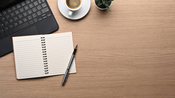 istock Above view empty notebook, pen, coffee cup and laptop on wooden table. 1355599468