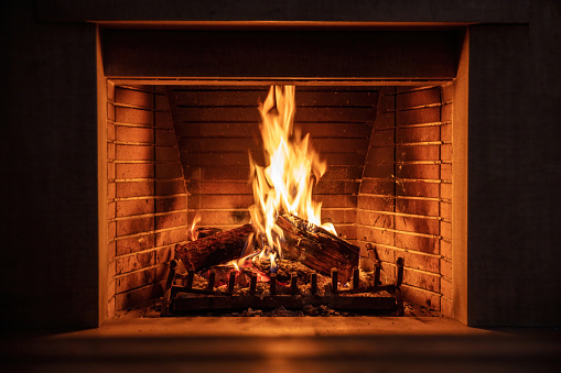 Fireplace burning firewood. Fire flames on wood logs, fireside bricks background. Cozy warm home at Christmas, dark room. Winter holidays greeting card