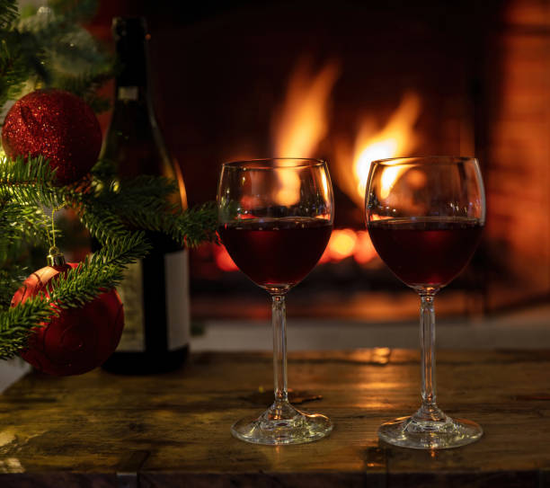 istock Red wine glasses, burning fireplace background. Christmas tree decoration 1355602788