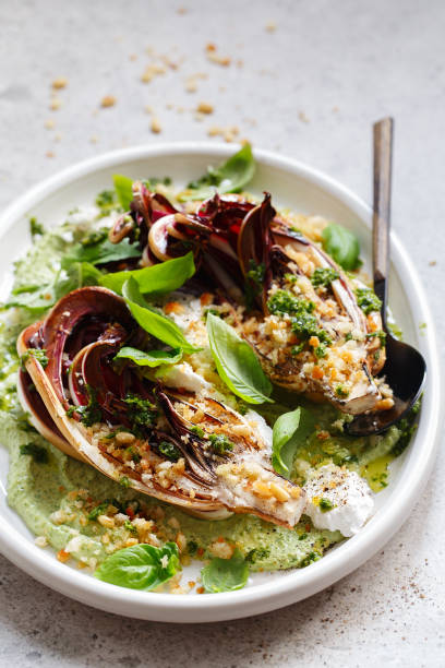 ensalada de radicchio asada con feta, tahini verde, piñones y pesto de albahaca. radicchio rosso di treviso tardivo, achicoria roja italiana. preparación de recetas de comidas saludables. platos a base de plantas. vida verde. - italian cuisine food preparing food cheese fotografías e imágenes de stock