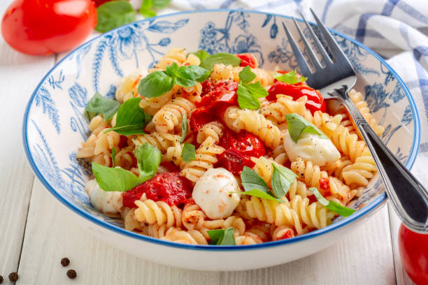 Pasta with baked caprese. Fusilli pasta with baked tomatoes, mozzarella and fresh basil in caprese style is served in a ceramic bowl. Top view. Concept of vegetarian nutrition. caprese salad stock pictures, royalty-free photos & images