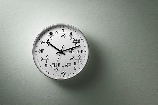 Maths clock magic 9. Clock with a dial, where hours are written using mathematics hanging on the wall.