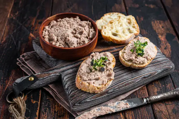 Photo of Toasts with Duck pate Rillettes de Canard on wooden board. Dark wooden background. Top View