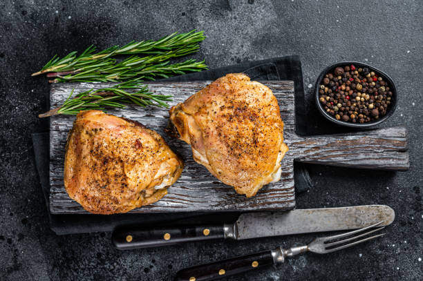 coxas de frango grelhadas em uma tábua de madeira com alecrim. fundo preto. vista superior - chicken thighs - fotografias e filmes do acervo