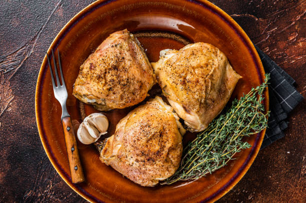 istock Roasted chicken thighs with spices in a plate. Dark background. Top View 1355614083
