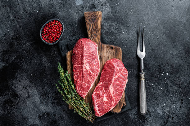 焼き生のトップブレードまたは平らな鉄の牛肉ステーキを肉屋のまな板に。黒の背景。トップビュー - chuck steak ストックフォトと画像