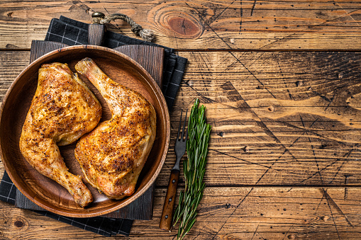 BBQ Grilled chicken legs in a wooden plate with herbs. wooden background. Top view. Copy space.