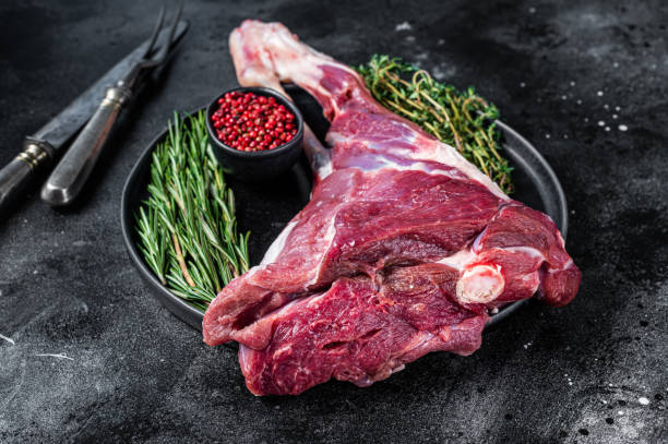istock Raw lamb mutton leg meat on the bone with herbs. Black background. Top view 1355617208
