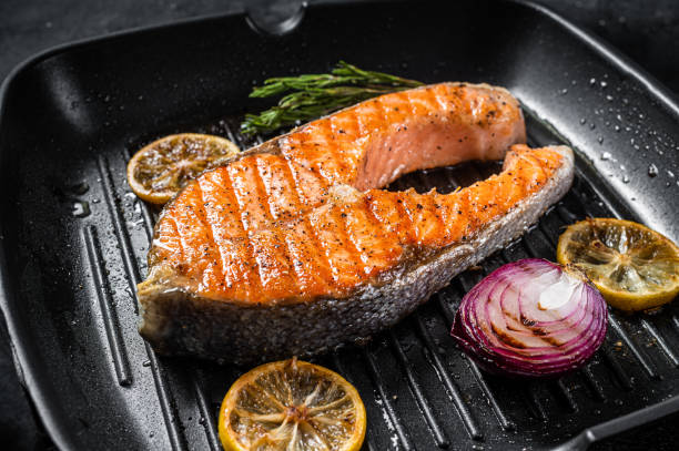 istock Salmon Fish Steak grilled on a grill pan with herbs. Black background. Top view 1355618452