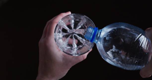 ludzkie ręce wlewają wodę do szklanki do picia. osobisty punkt widzenia na czarnym tle - water water bottle glass pouring zdjęcia i obrazy z banku zdjęć