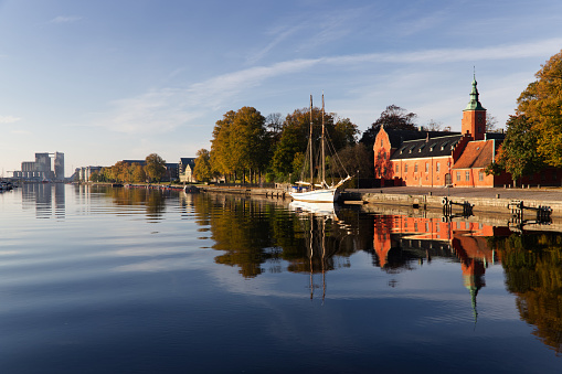 Halmstad, Halland, Sweden - October 10, 2021: Image was taken on the midday of the 10th of October from main city bridge towards one of the most famous places in city - the castle (Halmstads slott). There is also an old boat at the river bank and nice reflection on the river. Scenic waves and blue sky.