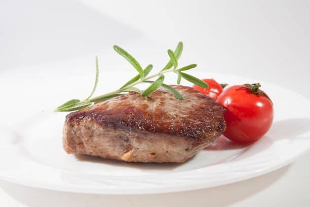 Appetizing steak well done on a white plate with tomatoes and rosemary