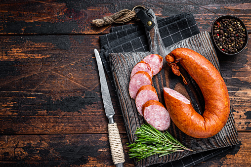 German Smoked sausage on a wooden rustic board with thyme. Dark wooden background. Top view. Copy space.