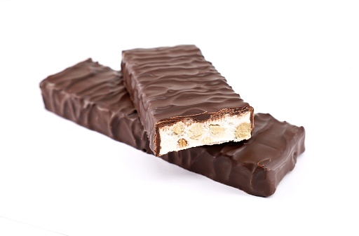 Two Torrone, one whole and the other cut, covered with dark chocolate on white background.  It is a traditional nougat of Italy\t.