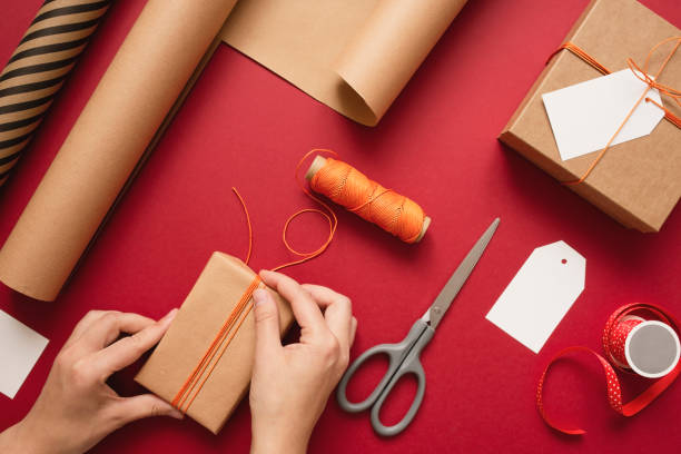 istock Young woman making bow on kraft gift boxe with orange thread on a red background. 1355625842