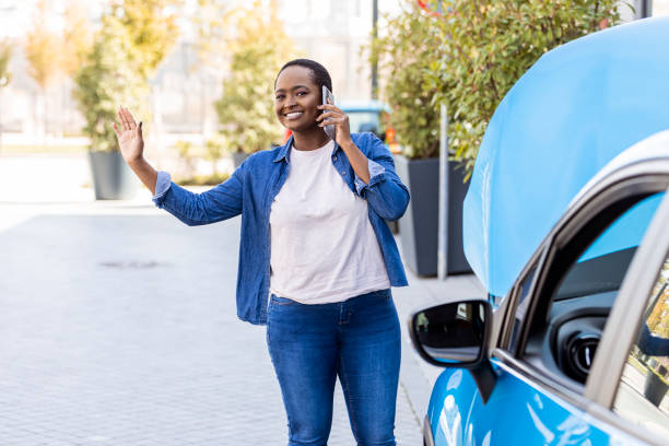 mulher sorridente chamando alguém para ajudar com seu carro quebrado. - roadside - fotografias e filmes do acervo