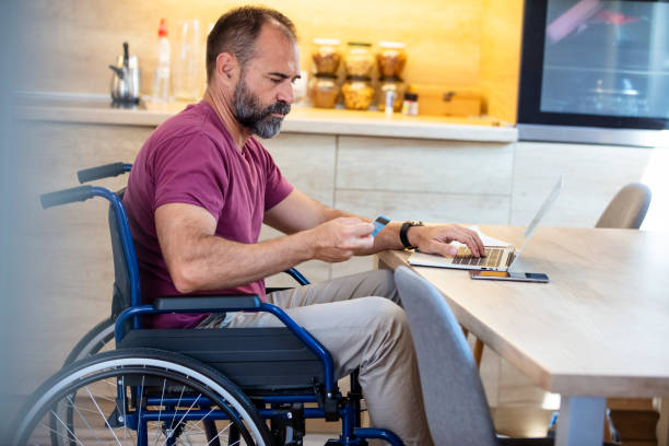 istock Businessman in a wheelchair analyzing paperwork while working at home. 1355632622