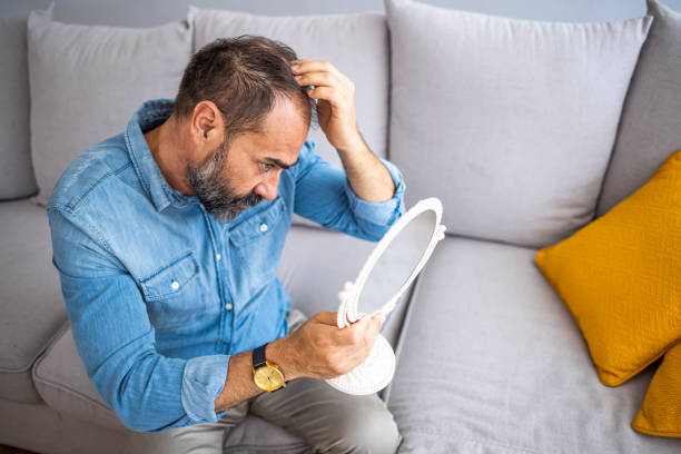 istock Man controls hair loss and unhappy looking in the mirror 1355632706