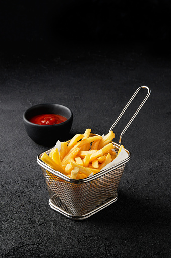 Fresh tasty french fries in basket with sauce on black background. Fastfood restaurant menu.
