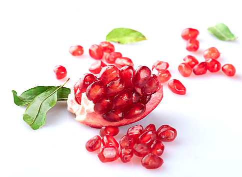 A piece of pomegranate with scattered grains and pomegranate leaves, isolated on a white background