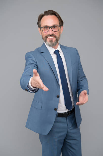 istock Extend a hand in a welcome gesture. handsome confident businessman. middle-aged man with eyeglasses. looking smart and intelligent. man with beard and glasses is confident. happy looking businessman 1355639854
