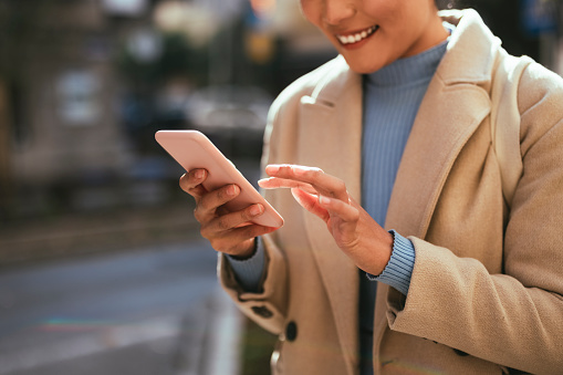 An anonymous Asian businesswoman typing text message while standing on the city street.