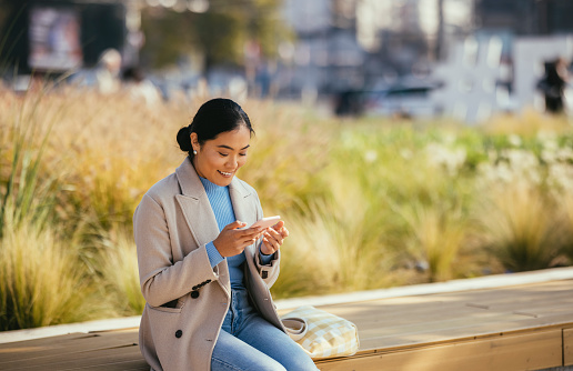 Smiling Asian Woman Sitting Outside and Looking at Her Phone