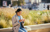 istock Smiling Asian Woman Sitting Outside and Looking at Her Phone 1355642927