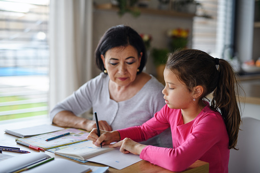 A small girl with grandmother doing homework indoors at home.
